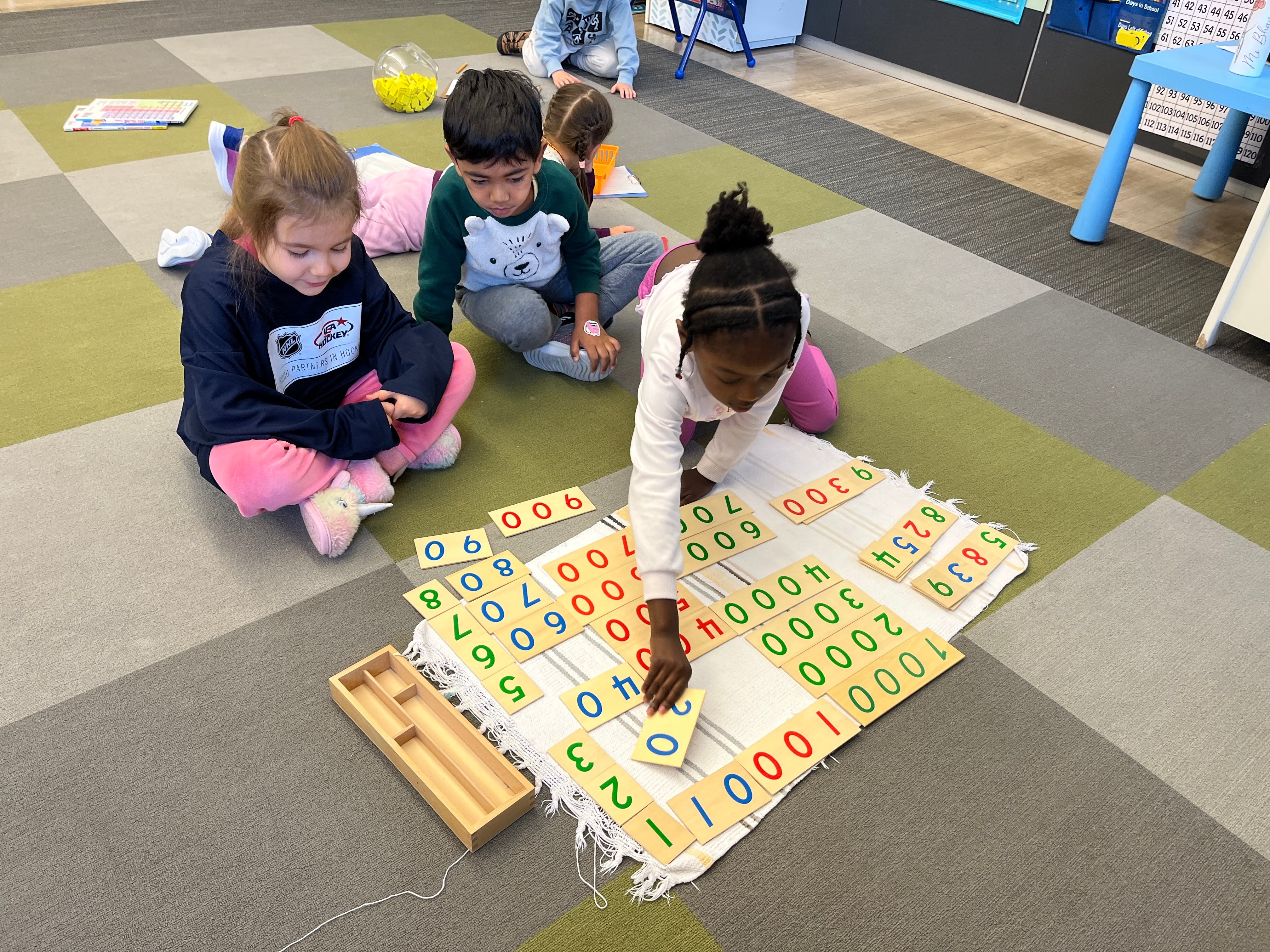 Children playing with educational number mats on a classroom floor.