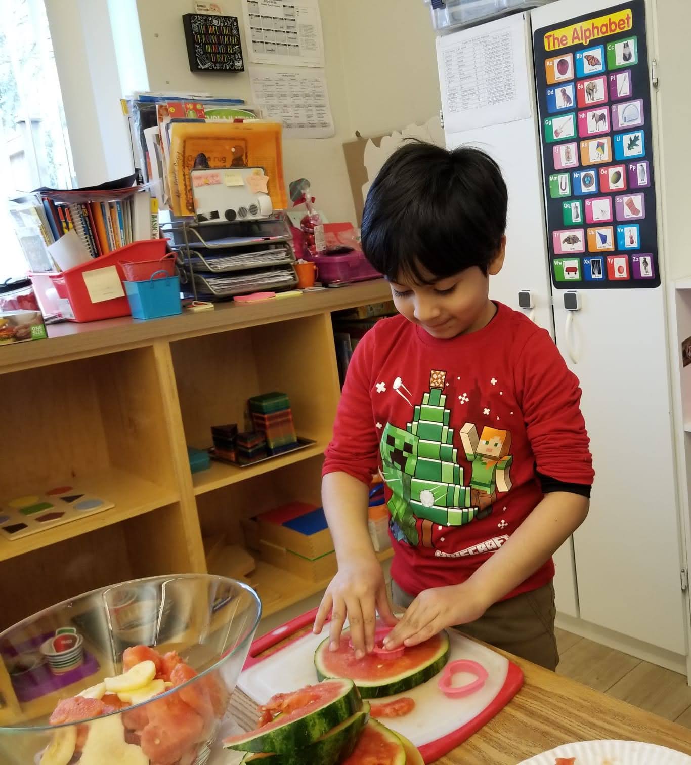 Child in a classroom setting cutting watermelon on a cutting board.
