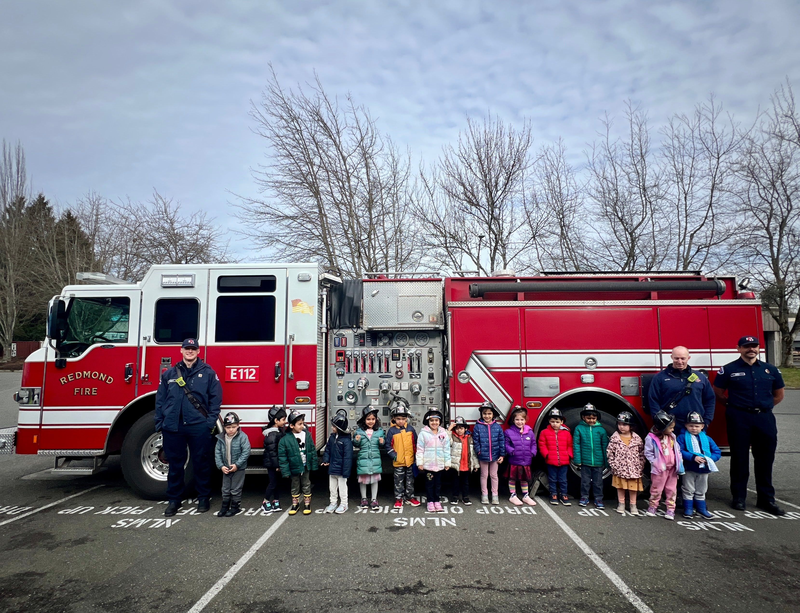 Children and adults standing in front of a fire truck on a cloudy day.