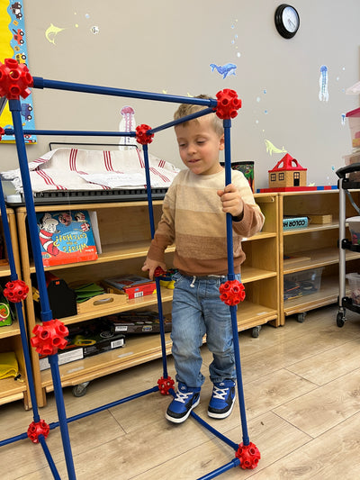 Child playing with a blue and red geometric toy set on a wooden floor.