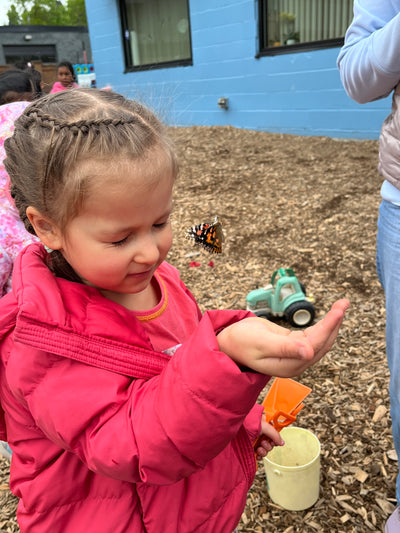 Child in a pink coat playing with toys on a gravel surface.