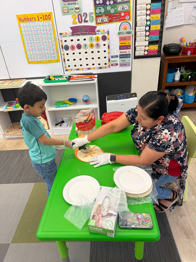 Two children at a green table with educational materials in a classroom setting.