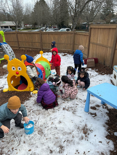 Children playing in a snowy playground with colorful equipment and a blue table.
